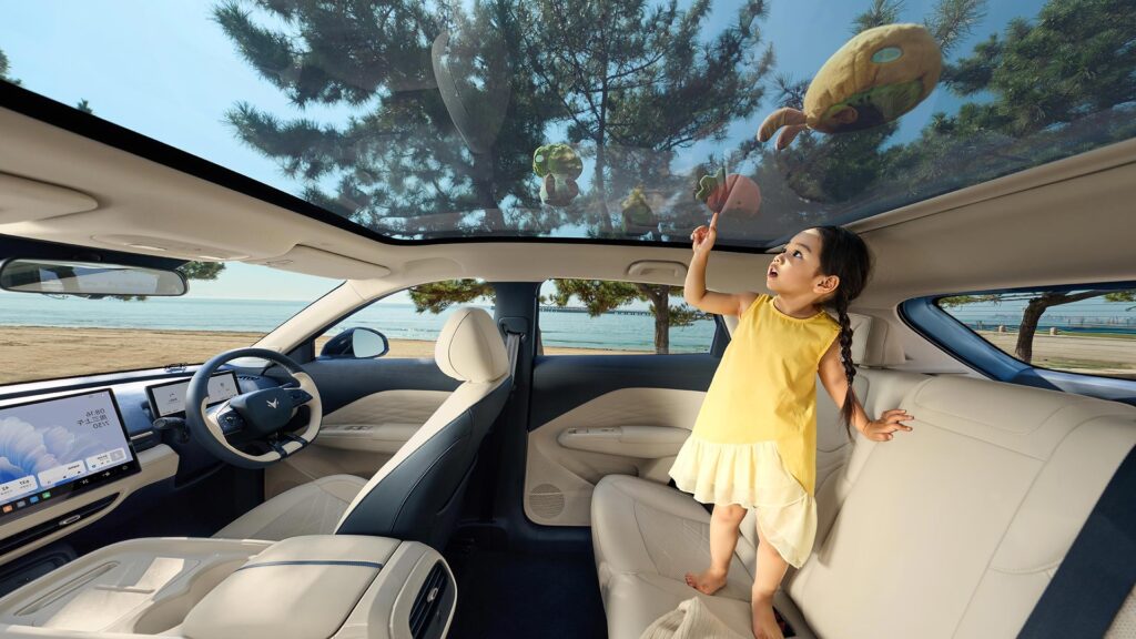 Young girl standing on the back seat of an all-electric ARCFOX T1 SUV looking up through the glass roof