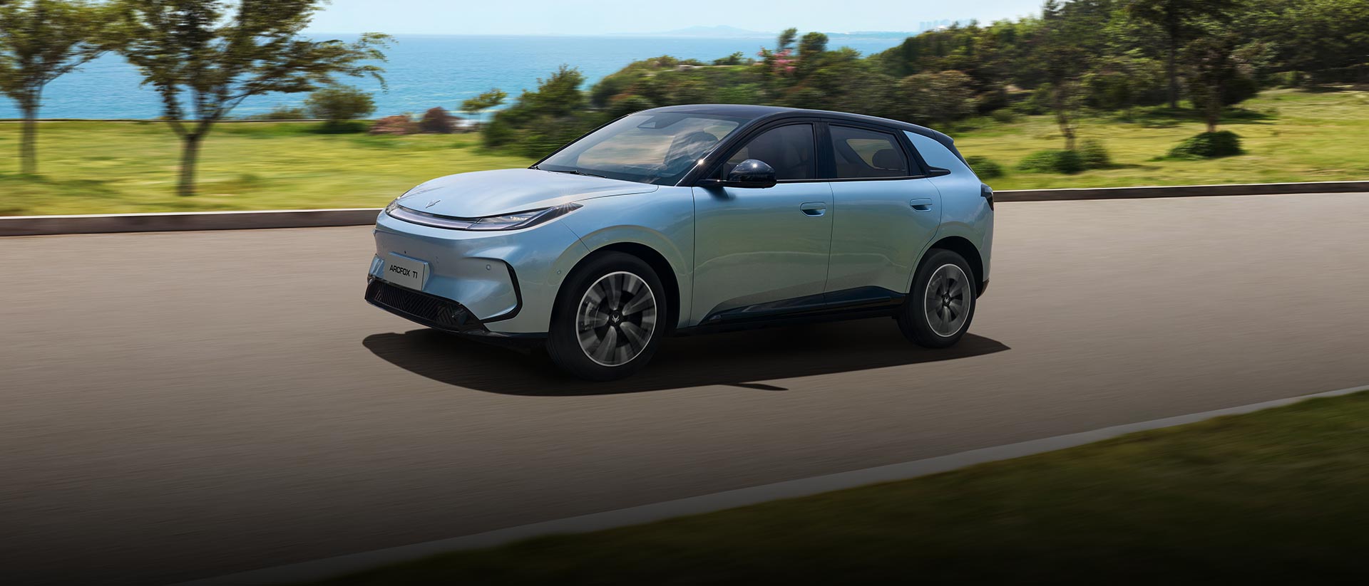 Front three quarter view of a blue ARCFOX T1 electric SUV driving by the ocean