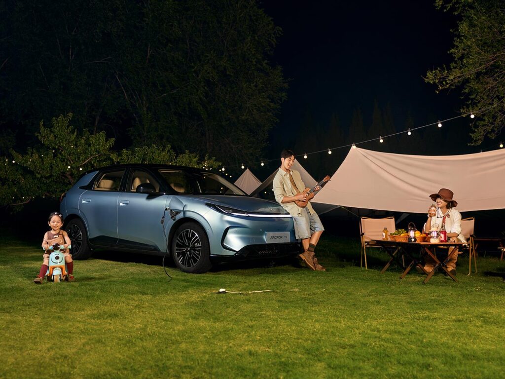 Front three quarter view of a blue ARCFOX T1 electric SUV parked next to a tent with the car providing power to the camp site