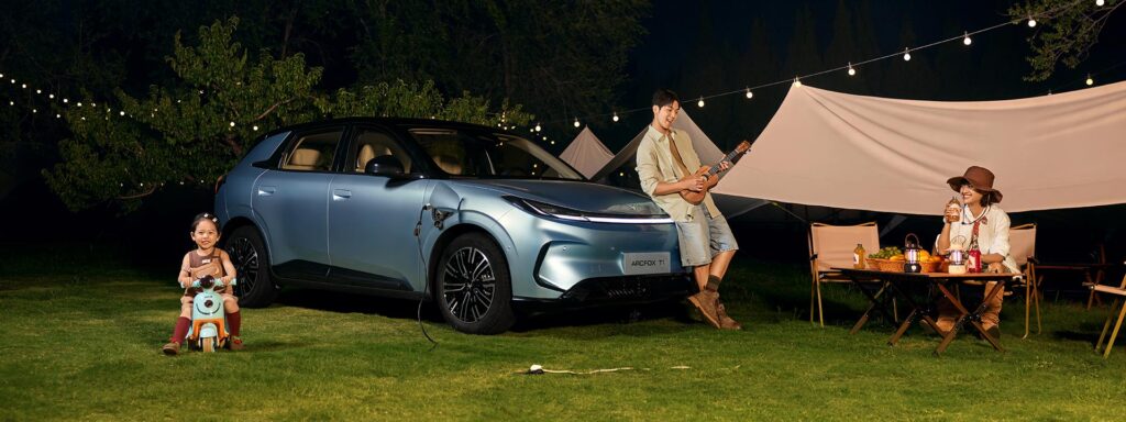 Front three quarter view of a blue ARCFOX T1 electric SUV parked next to a tent with the car providing power to the camp site